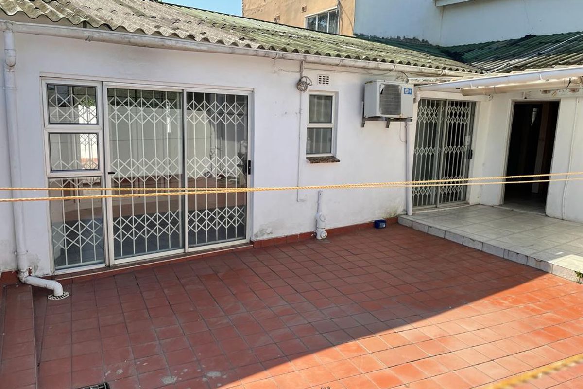 Rear exterior view of the property featuring a tiled patio area, sliding glass doors with security gates, and an external air conditioning unit.