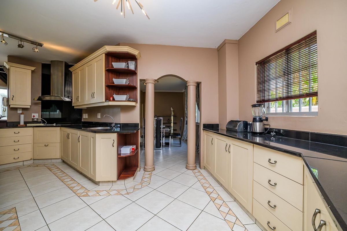 Spacious kitchen featuring cream cabinetry, black granite countertops, stainless steel extractor fan, and tiled flooring with decorative inlay, leading to an adjacent dining area.