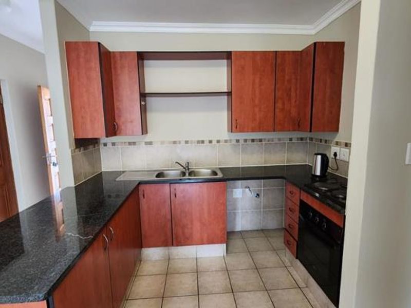 A functional kitchen featuring cherry-wood cabinetry, granite countertops, a double bowl sink, and built-in oven with hob, finished with neutral tiled flooring and backsplash.