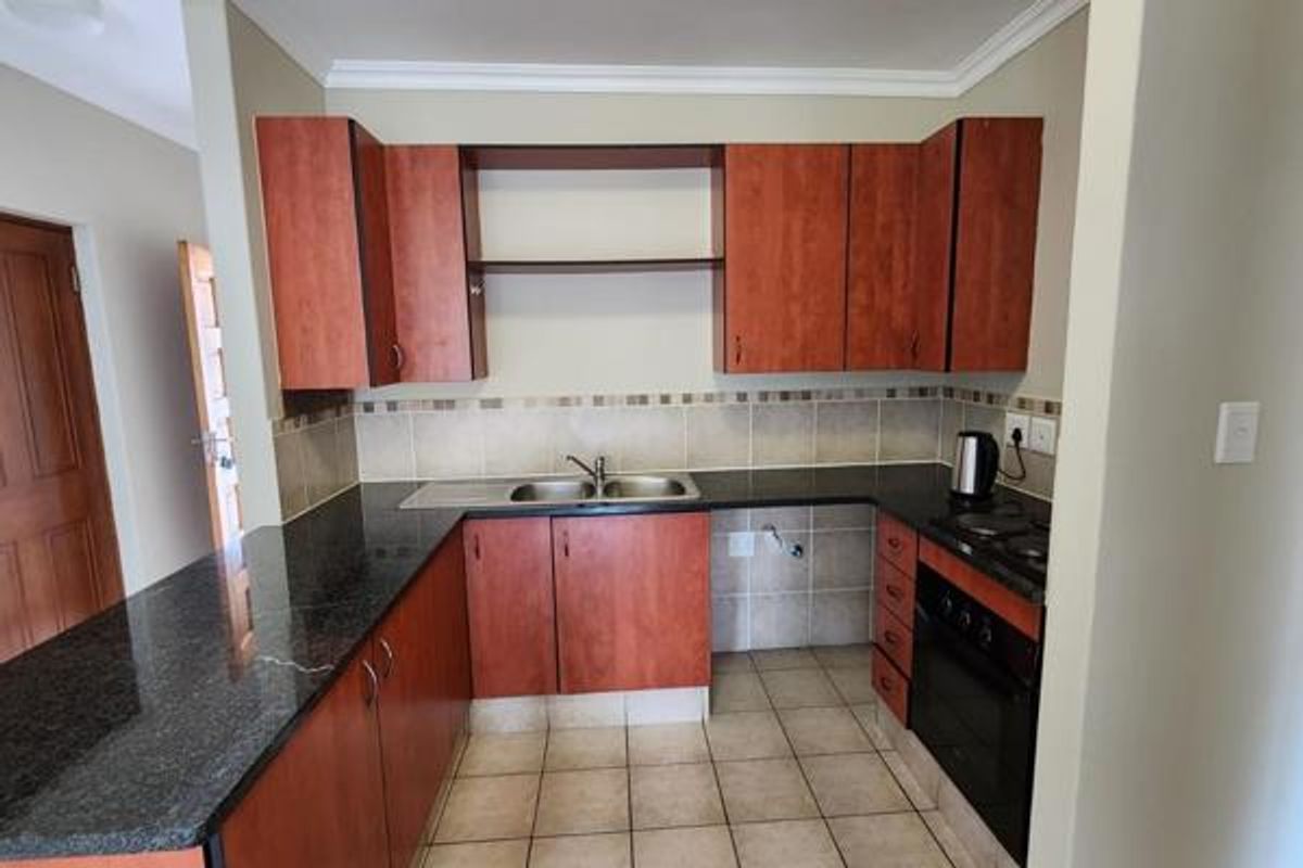 A functional kitchen featuring cherry-wood cabinetry, granite countertops, a double bowl sink, and built-in oven with hob, finished with neutral tiled flooring and backsplash.