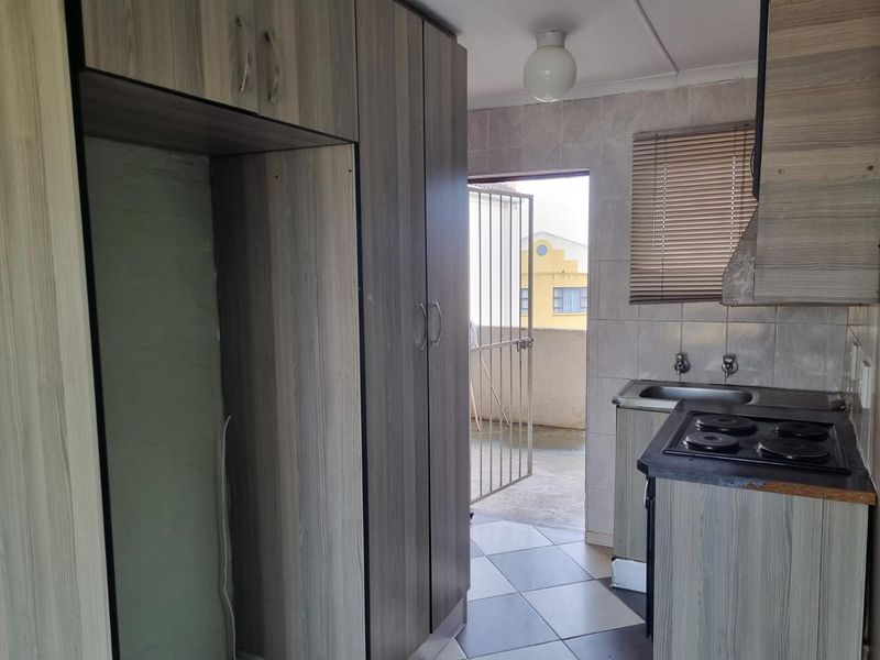 A compact kitchen featuring wood-look cabinetry, a built-in hob with extractor, tiled backsplash, and direct access to an outdoor balcony area.