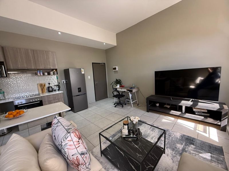 Modern open-plan living area featuring a well-appointed kitchen with built-in cabinetry, tiled flooring, and recessed lighting, seamlessly flowing into the lounge space.