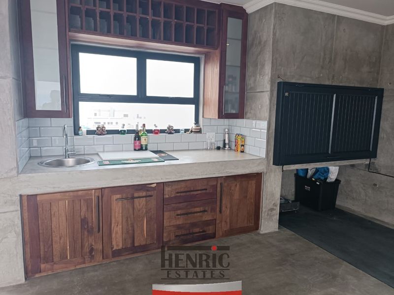 A modern bar area featuring custom wood cabinetry, a concrete countertop with integrated sink, subway tile backsplash, and a built-in braai.