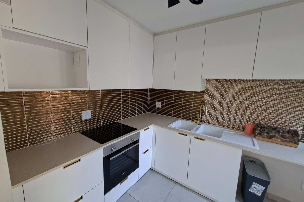 Modern kitchen featuring white cabinetry, stone countertops, integrated electric hob and oven, and a double basin sink with a tiled backsplash.