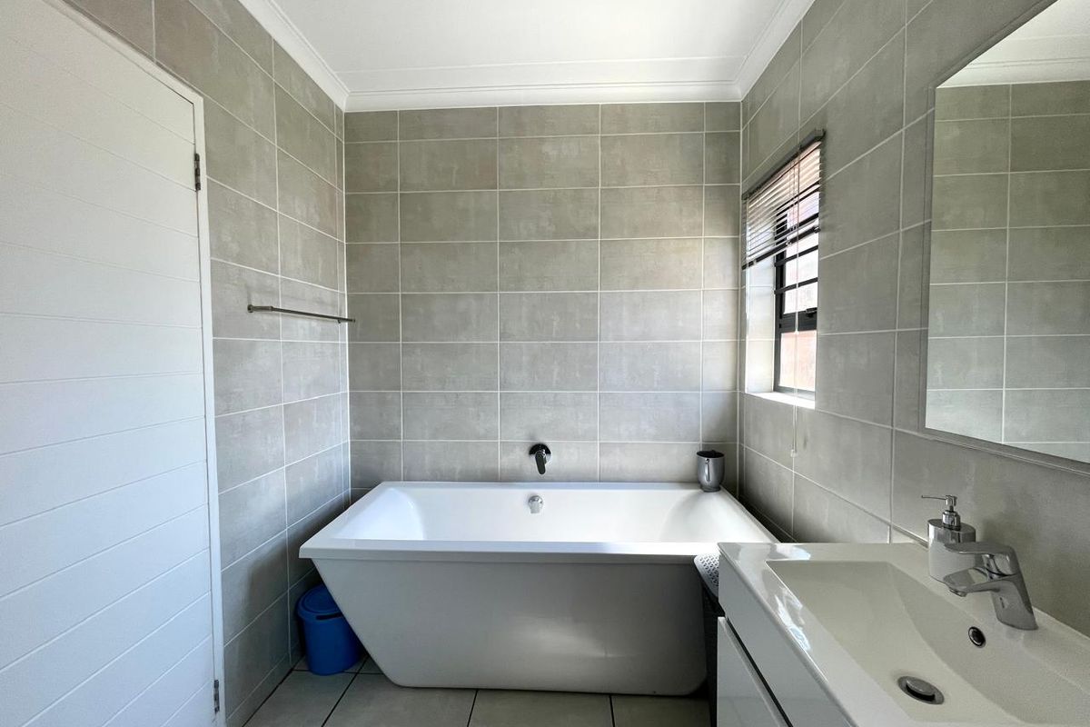 A modern bathroom featuring a freestanding bathtub, wall-mounted faucet, and a sleek vanity with a basin, finished with neutral grey wall and floor tiles.