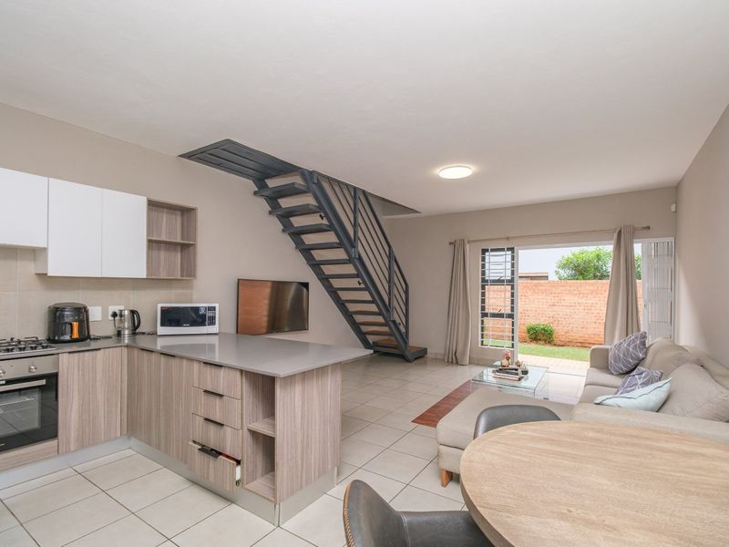 Open-plan living area featuring a modern kitchen with built-in appliances, a metal staircase, and direct access to the rear garden through sliding doors.