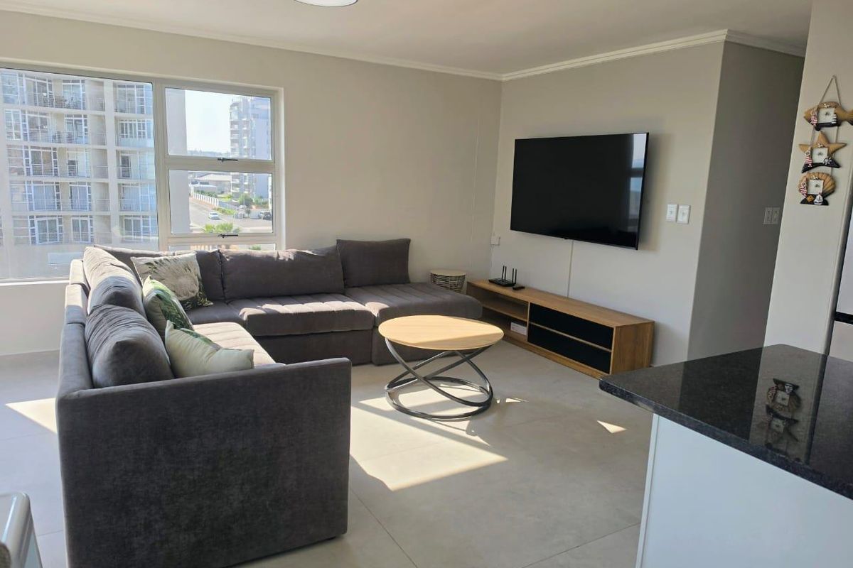 A bright and modern living room featuring large aluminium windows, neutral tiled flooring, and clean finishes, offering a comfortable and well-maintained living space.