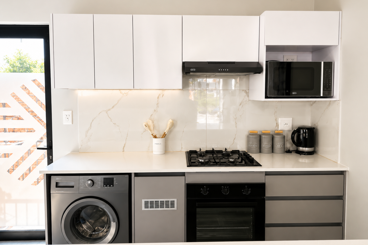 Modern kitchen featuring sleek white cabinetry, marble-look splashback, built-in gas hob, oven, extractor fan, and integrated washing machine.