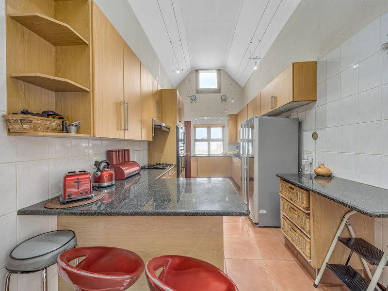 A functional kitchen featuring granite countertops, light wood cabinetry, tiled backsplash, and a high vaulted ceiling with ample storage space.