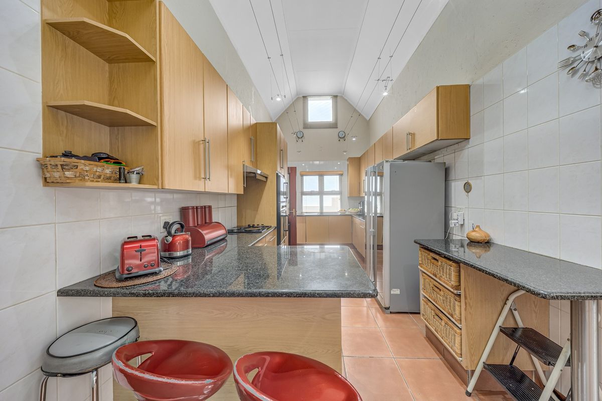 A functional kitchen featuring granite countertops, light wood cabinetry, tiled backsplash, and a high vaulted ceiling with ample storage space.