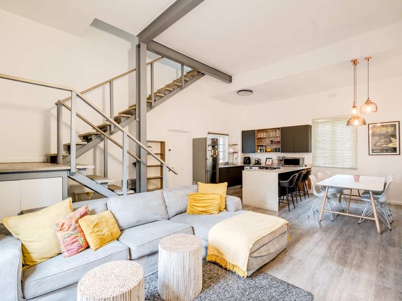 Spacious open-plan living area featuring a modern kitchen with island, dining space, and a striking industrial-style steel staircase leading to the upper level.