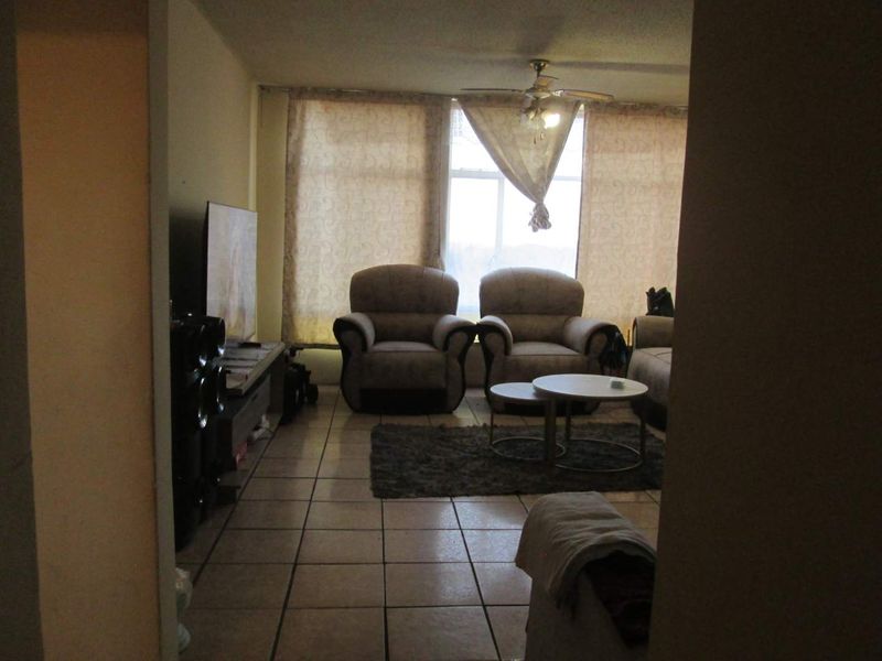 A living room area featuring tiled flooring, a ceiling fan, and a large window providing natural light.