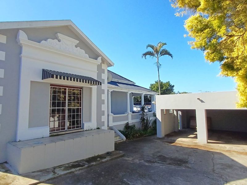Front view of a classic house featuring a decorative gable, a covered veranda with columns, and an attached carport with a concrete driveway.