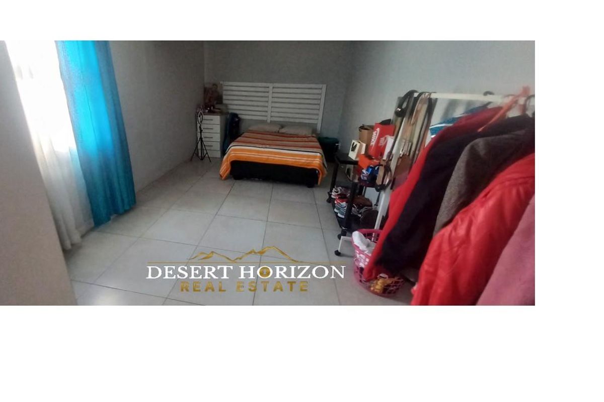A spacious bedroom featuring neutral tiled flooring and a large window, providing a functional and well-lit living space.