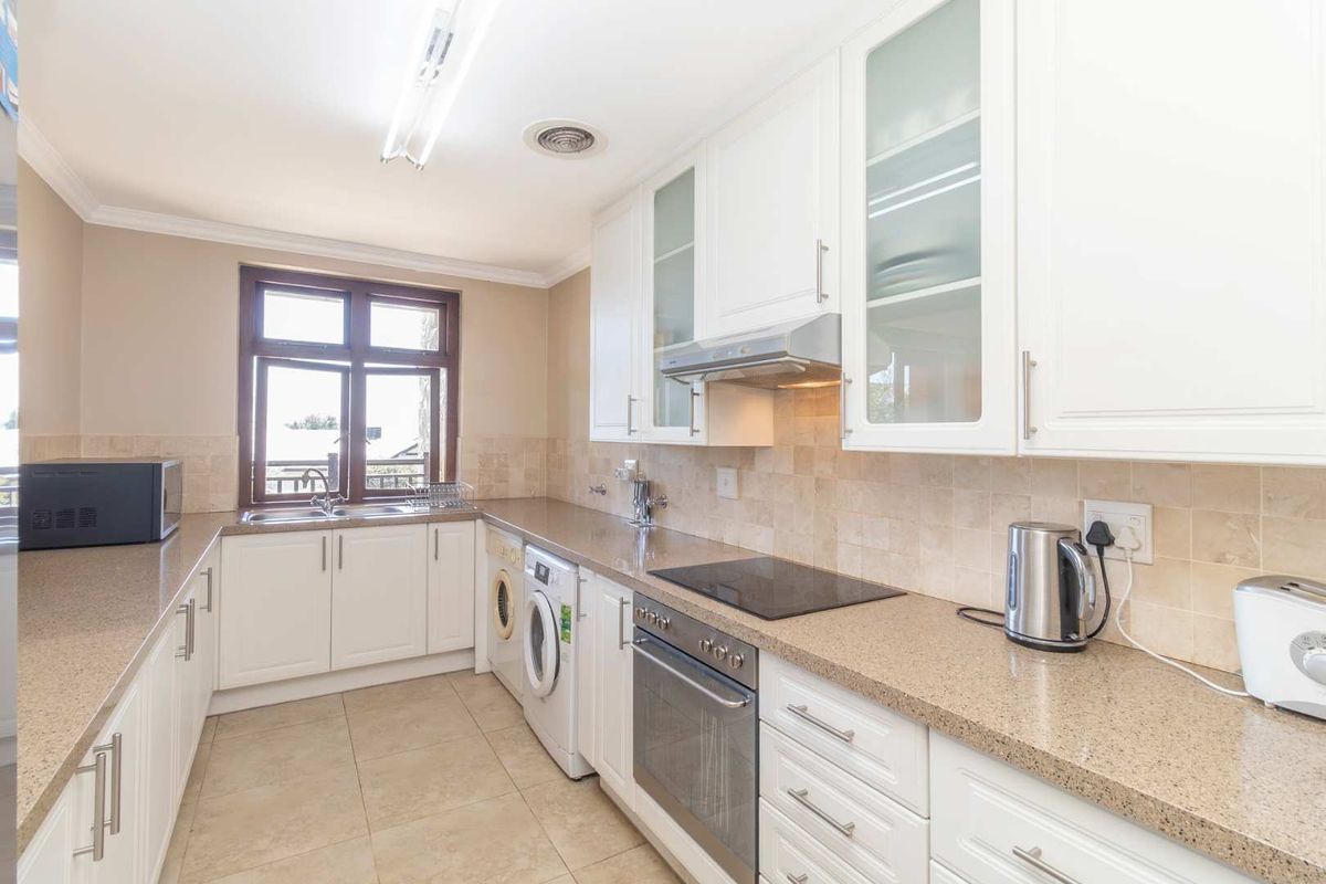 A functional kitchen featuring white cabinetry, stone-look countertops, a built-in oven, hob, extractor fan, and integrated laundry appliance space.