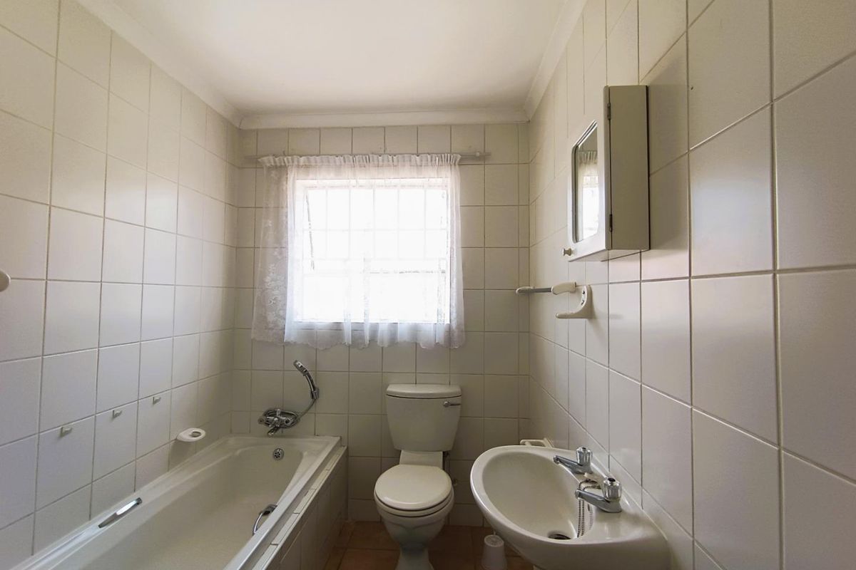 A functional bathroom featuring a standard bathtub, pedestal basin, and toilet with full-height wall tiling and a window for natural light.