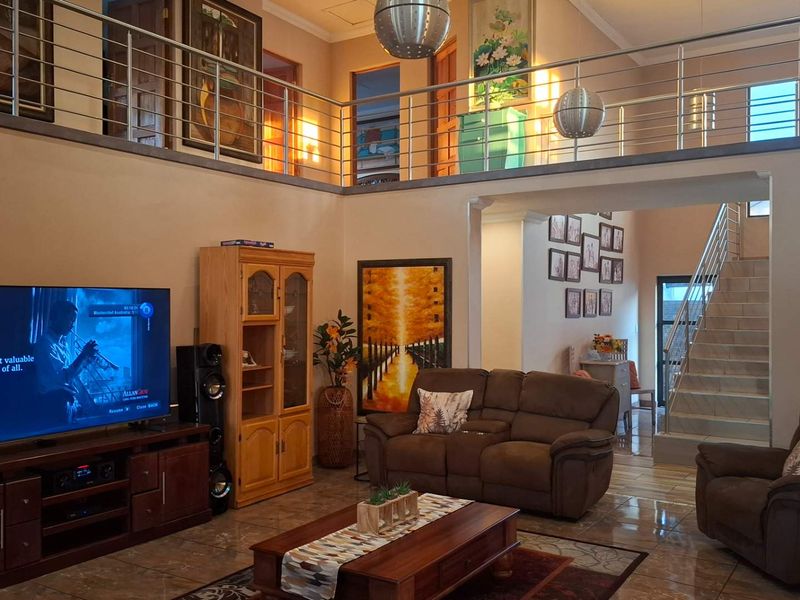 Spacious double-volume living room featuring a mezzanine level with stainless steel balustrades, tiled flooring, and an open-plan staircase.