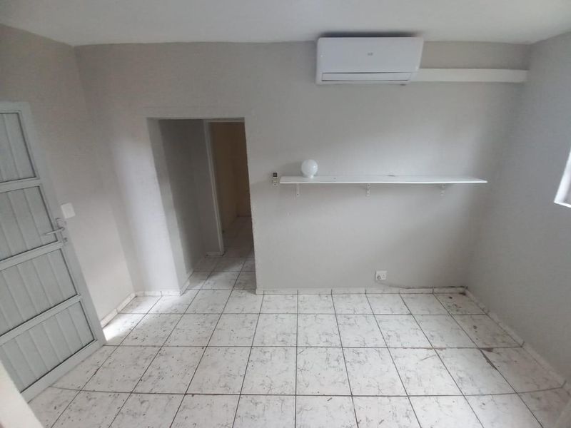 An empty bedroom featuring tiled flooring, a wall-mounted shelf, and a split-system air conditioning unit.