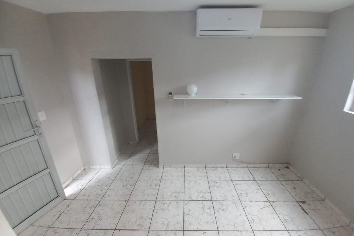 An empty bedroom featuring tiled flooring, a wall-mounted shelf, and a split-system air conditioning unit.