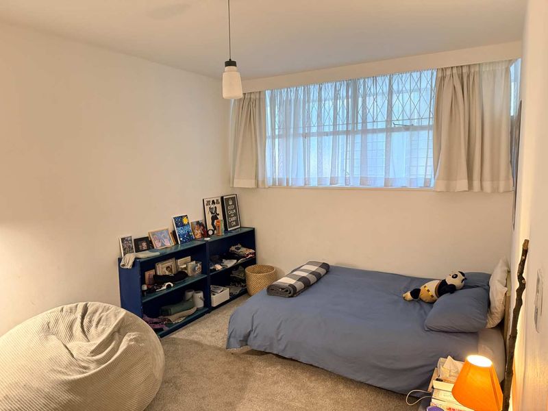 A functional bedroom featuring carpeted flooring, a large window with security bars, and a central pendant light fixture.
