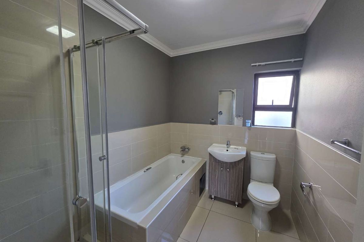 A modern bathroom featuring a tiled bathtub, a separate glass-enclosed shower, a vanity basin, and a toilet with neutral wall and floor tiles.