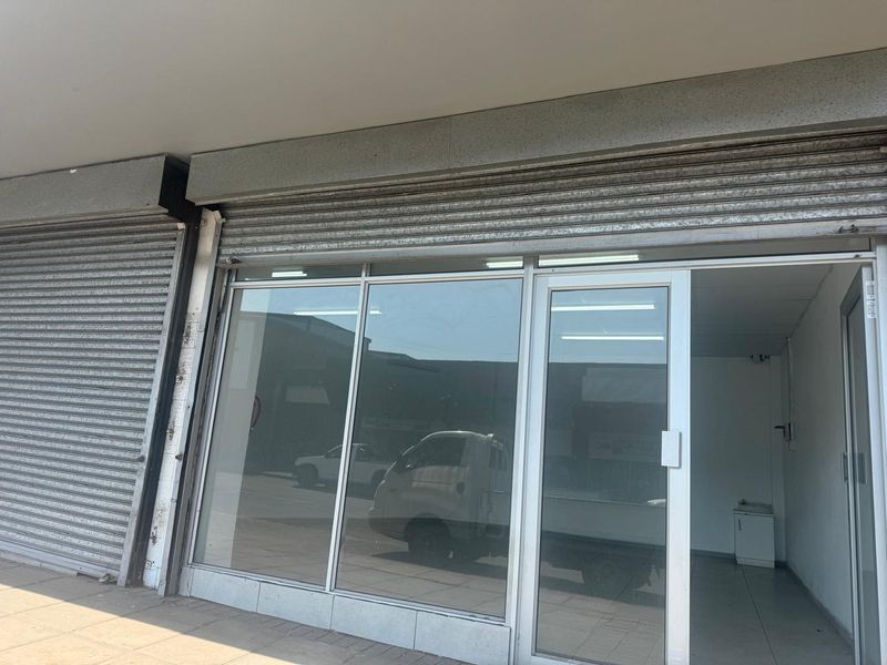 Front facade of a retail unit featuring a large glass storefront, aluminium entrance door, and secure metal roller shutters.