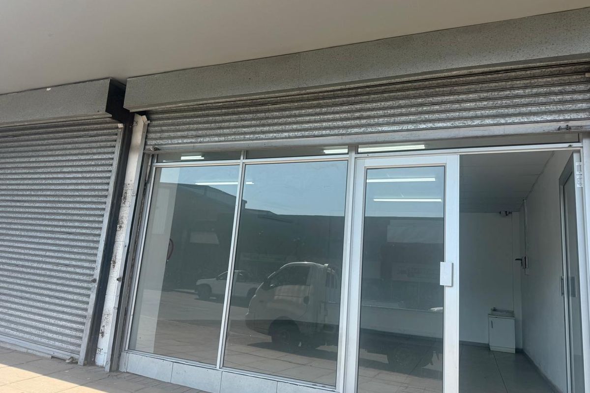 Front facade of a retail unit featuring a large glass storefront, aluminium entrance door, and secure metal roller shutters.