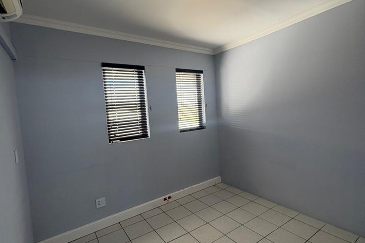 A clean, empty office space featuring tiled flooring, split-system air conditioning, and dual windows with fitted venetian blinds.