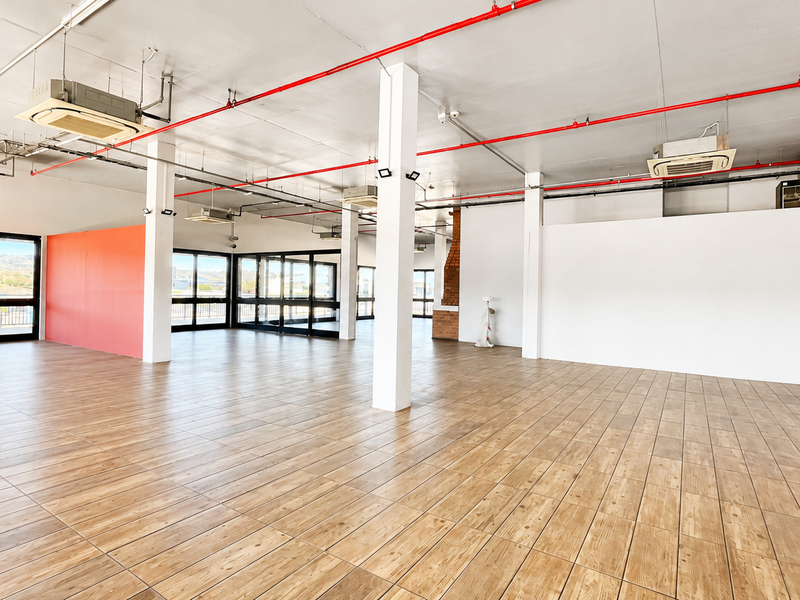 Spacious open-plan retail area featuring wood-look tile flooring, exposed fire sprinkler piping, ceiling-mounted air conditioning, and large glass doors providing ample natural light.