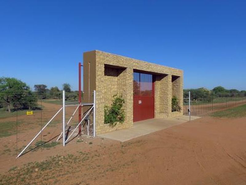 A secure farm entrance featuring a stone-clad pillar structure with a central metal gate and perimeter wire fencing.