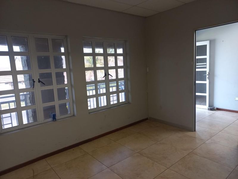 An empty office space featuring tiled flooring, grid windows, and a drop ceiling, providing a neutral environment suitable for various business configurations.