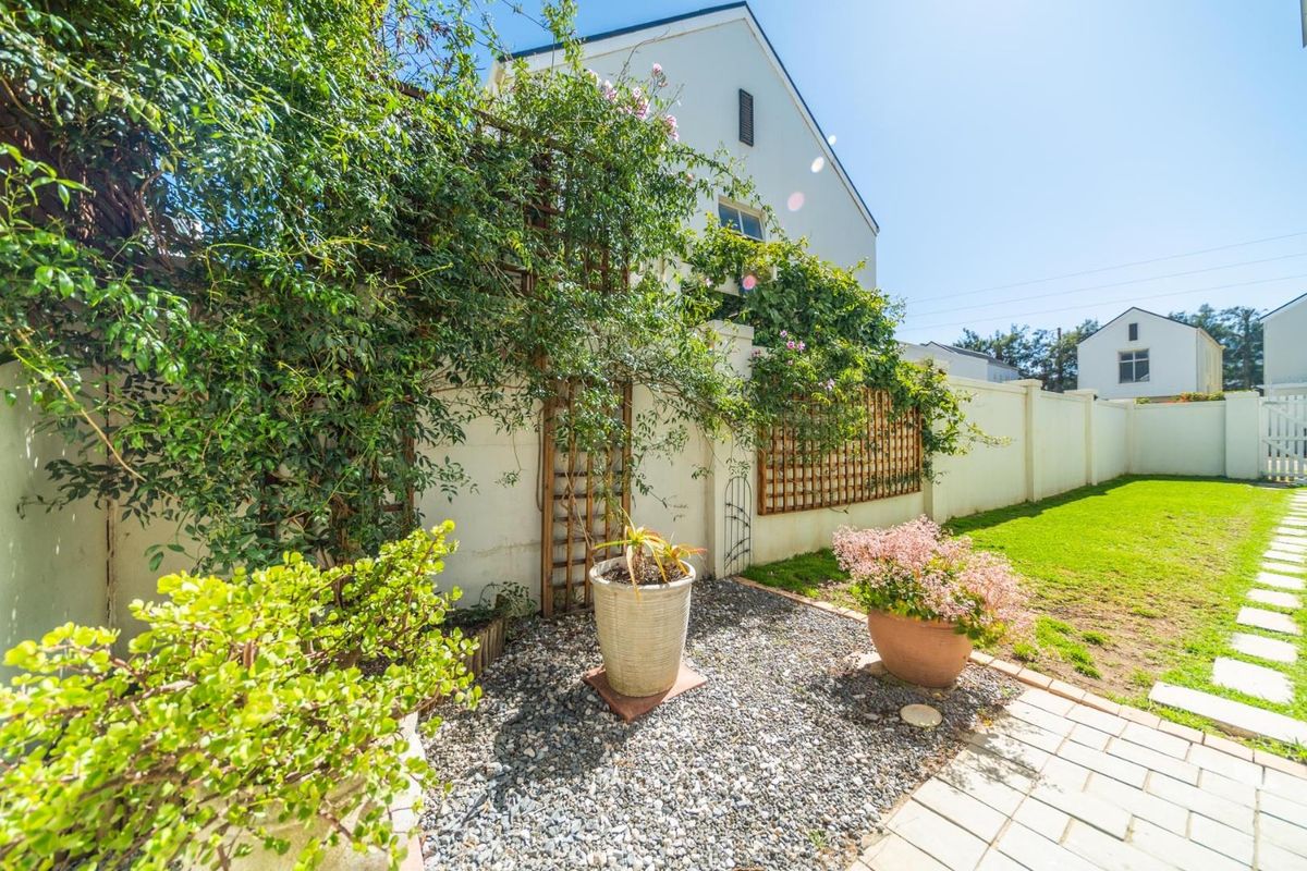 A private rear garden featuring a paved walkway, gravel area, established climbing plants on trellis, and a well-maintained lawn.
