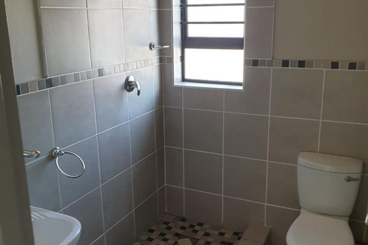 A functional bathroom featuring a walk-in shower, toilet, and basin with neutral wall and floor tiling.
