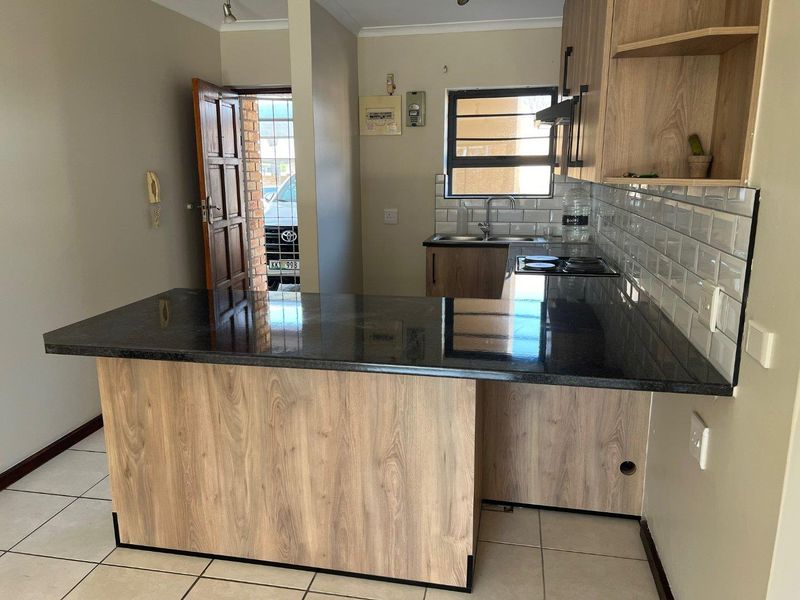 A modern kitchen featuring wood-look cabinetry, dark granite countertops, a subway tile backsplash, and an integrated electric hob with an extractor fan.