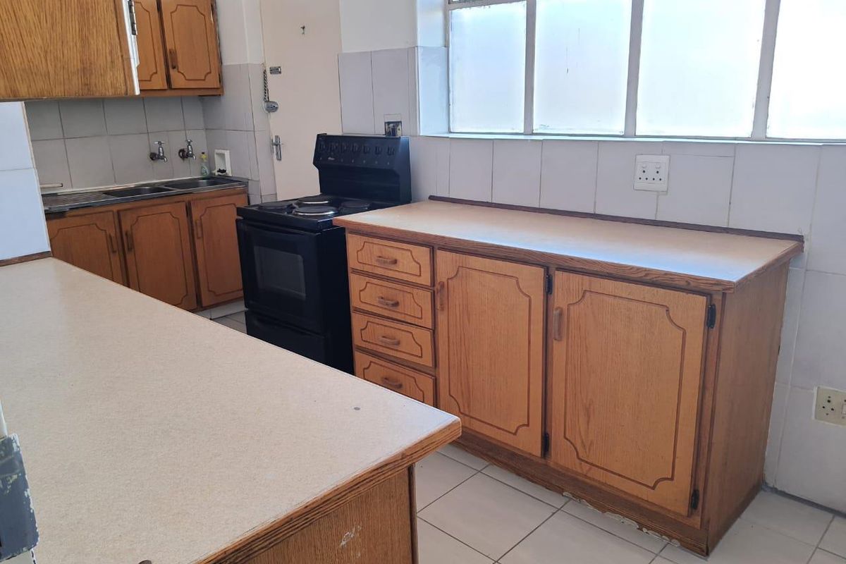 A functional kitchen featuring dated wooden cabinetry, laminate countertops, tiled flooring, and a freestanding stove, offering potential for a modern renovation.