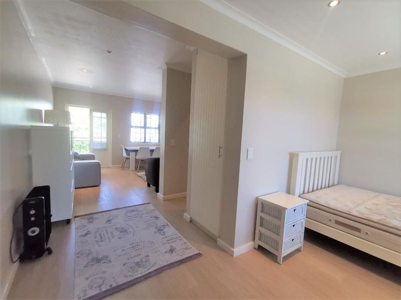 Open-plan living area featuring light laminate flooring, recessed downlighting, and a built-in cupboard, with direct access to a balcony through a sliding glass door.