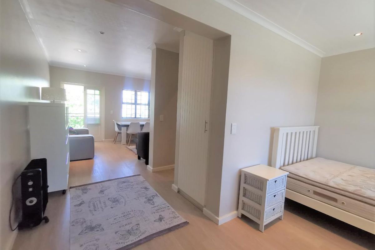 Open-plan living area featuring light laminate flooring, recessed downlighting, and a built-in cupboard, with direct access to a balcony through a sliding glass door.