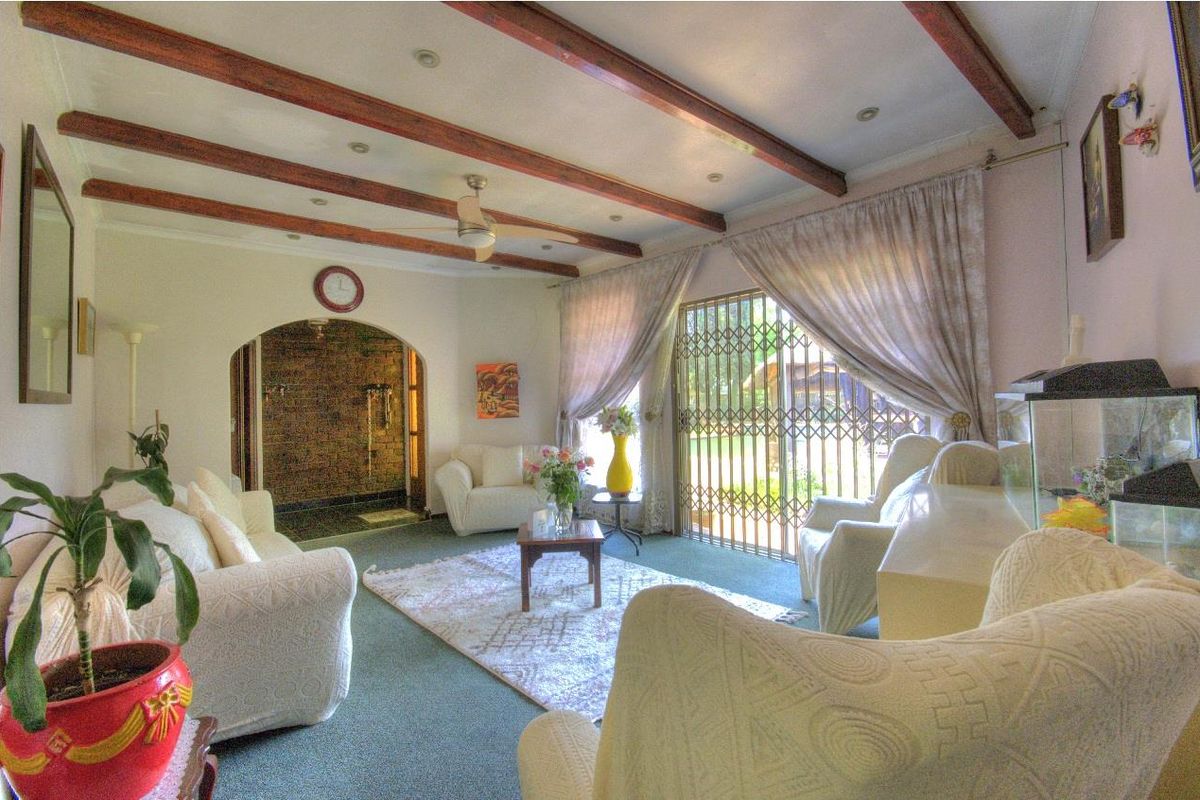 A living room featuring exposed timber ceiling beams, a ceiling fan, and an arched entryway leading to an adjacent space with a sliding security door.