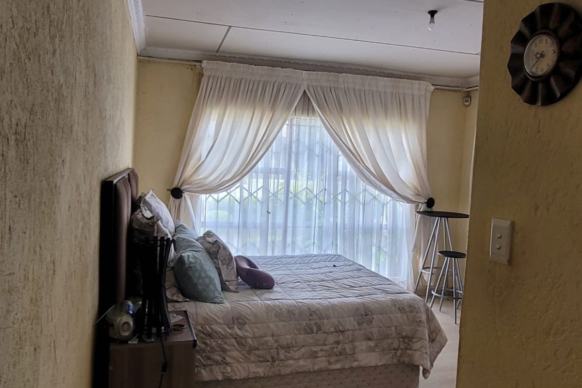 A bedroom featuring textured walls, a large window with security gate, and ceiling cornice detailing, requiring cosmetic updates to improve the overall finish.
