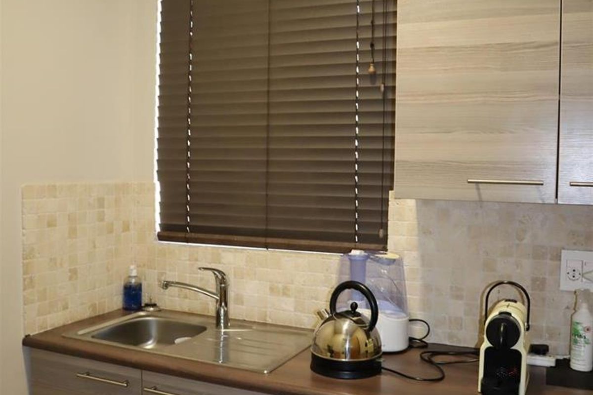 A compact kitchen area featuring modern wood-grain cabinetry, a stainless steel sink, tiled backsplash, and functional laminate countertops.