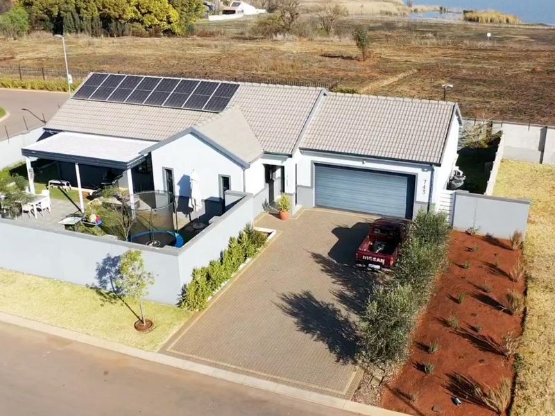 Aerial view of a modern residential property featuring a paved driveway, garage, covered patio, and roof-mounted solar panels.