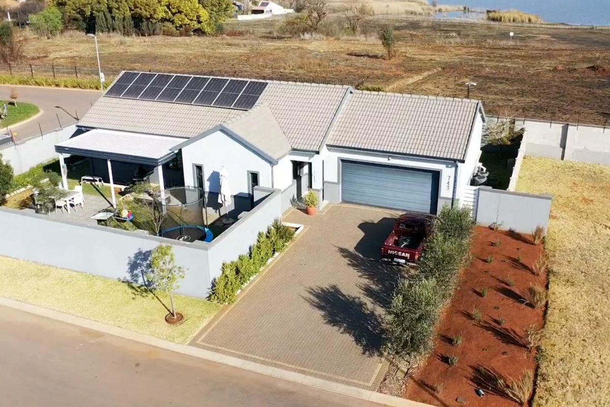Aerial view of a modern residential property featuring a paved driveway, garage, covered patio, and roof-mounted solar panels.