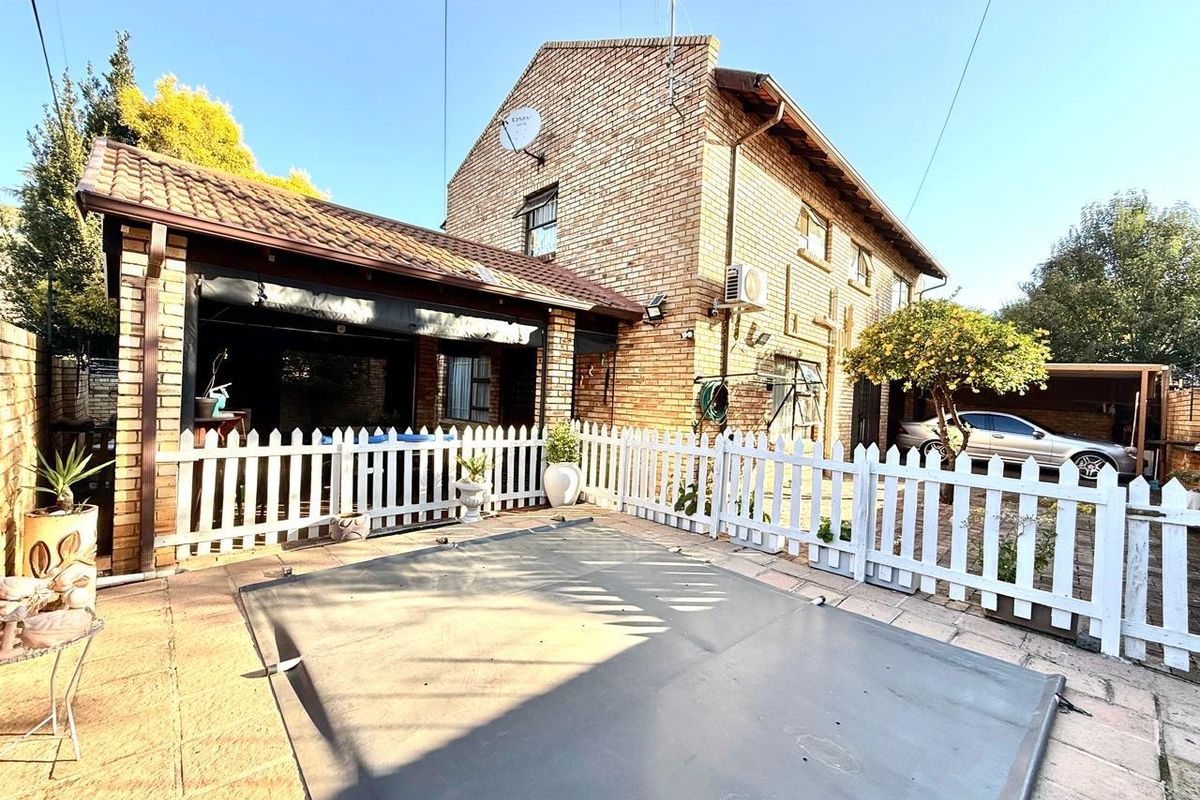 Rear exterior view of the cluster home featuring a covered patio, a swimming pool with a safety cover, and a white picket fence.