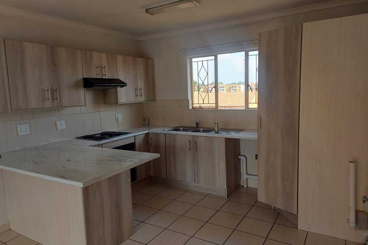 Functional kitchen featuring light wood-look cabinetry, marble-effect countertops, built-in hob with extractor, and tiled flooring in a clean, vacant space.