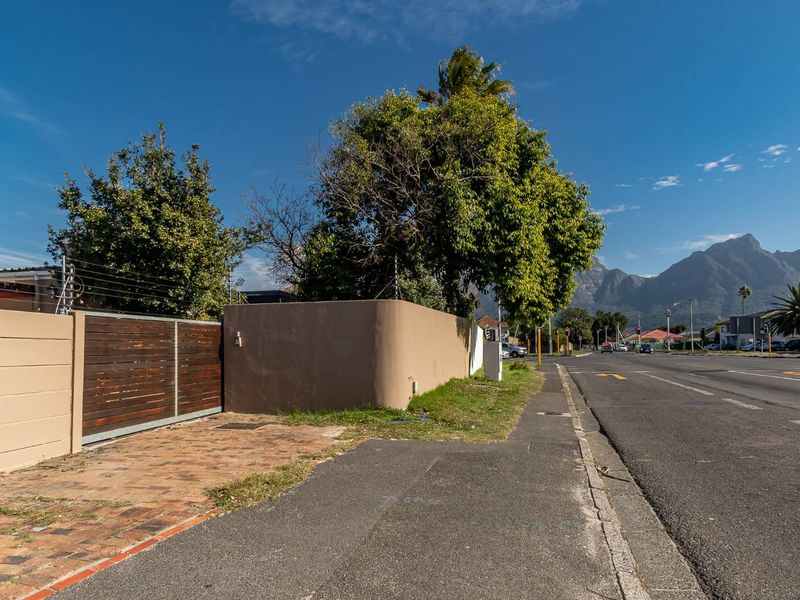 Street view showing the property boundary wall, electric fencing, and sliding gate access from the sidewalk.