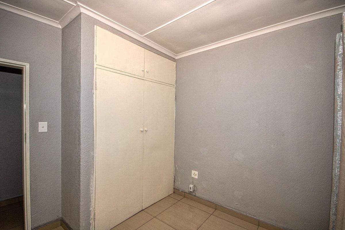 An empty bedroom featuring tiled flooring, a built-in cupboard, and grey textured walls, offering a blank canvas for renovation or interior design.