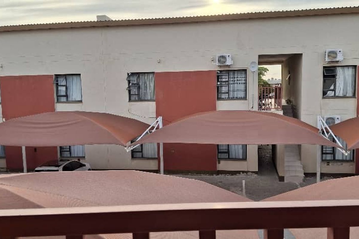 Exterior view of an apartment complex featuring shaded parking bays and multi-story residential units with metal-framed windows.
