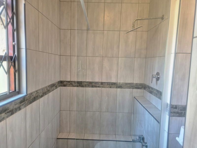 A clean, modern bathroom shower enclosure featuring neutral wall tiles, a glass screen, and a built-in shower niche for storage.