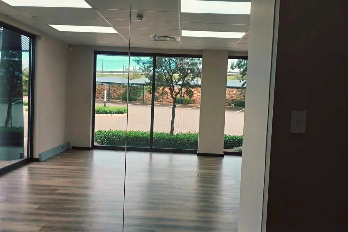 Modern, bright office space featuring laminate flooring, a suspended ceiling with recessed lighting, and large glass sliding doors overlooking the parking area.