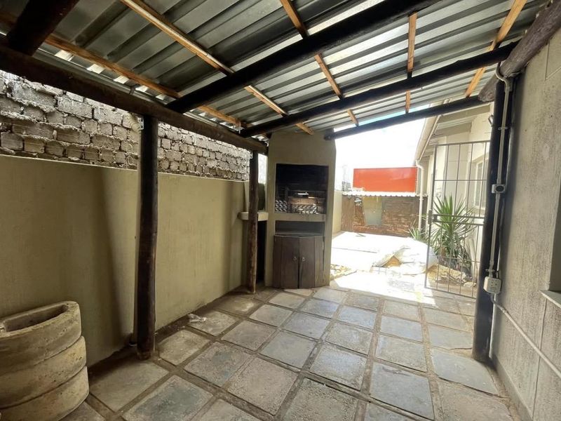 Covered outdoor patio area featuring a built-in braai, paved flooring, and timber structural supports, offering a functional space for outdoor entertaining.